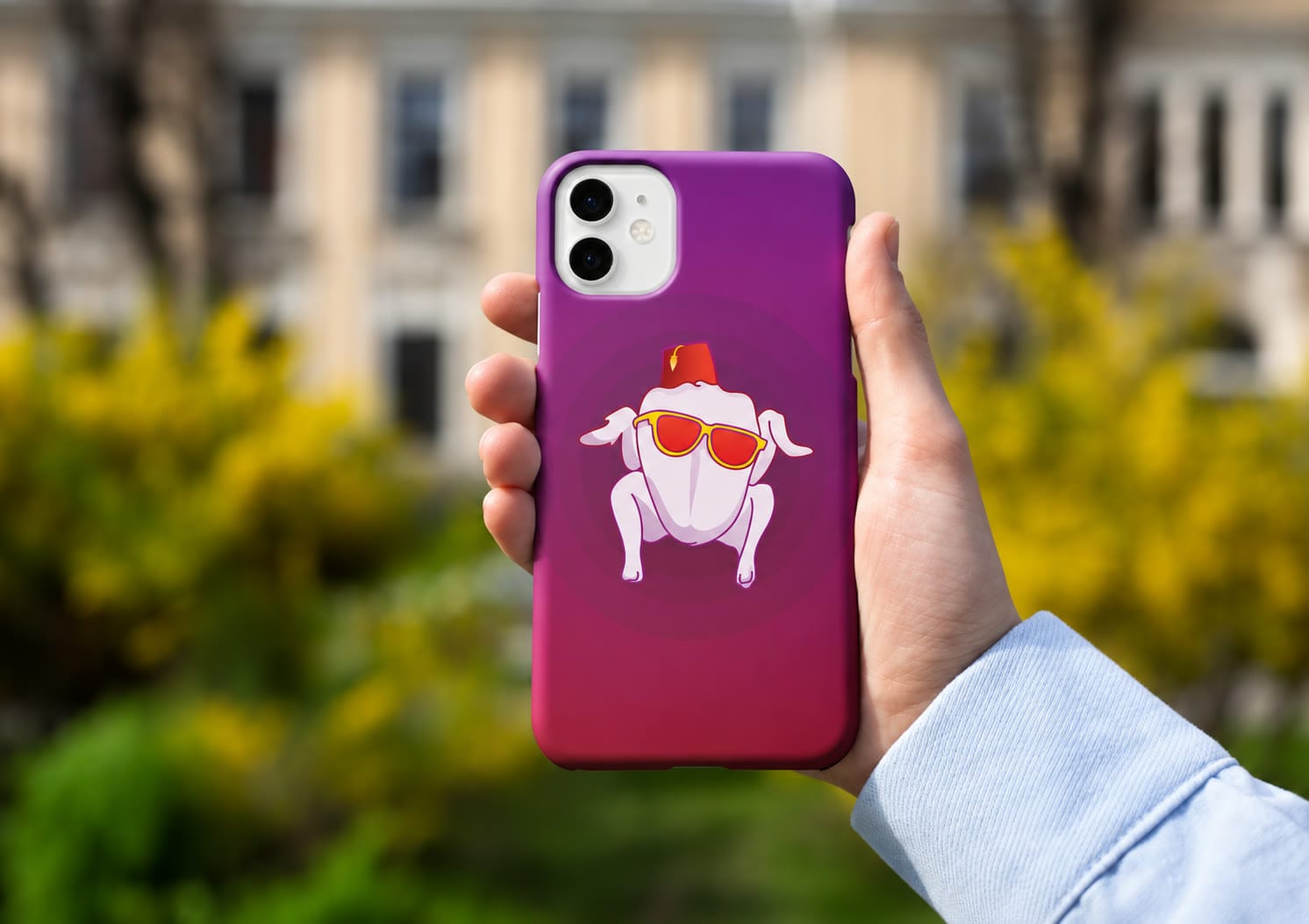 A magenta Our Case phone case held up in front of a garden and a stone building