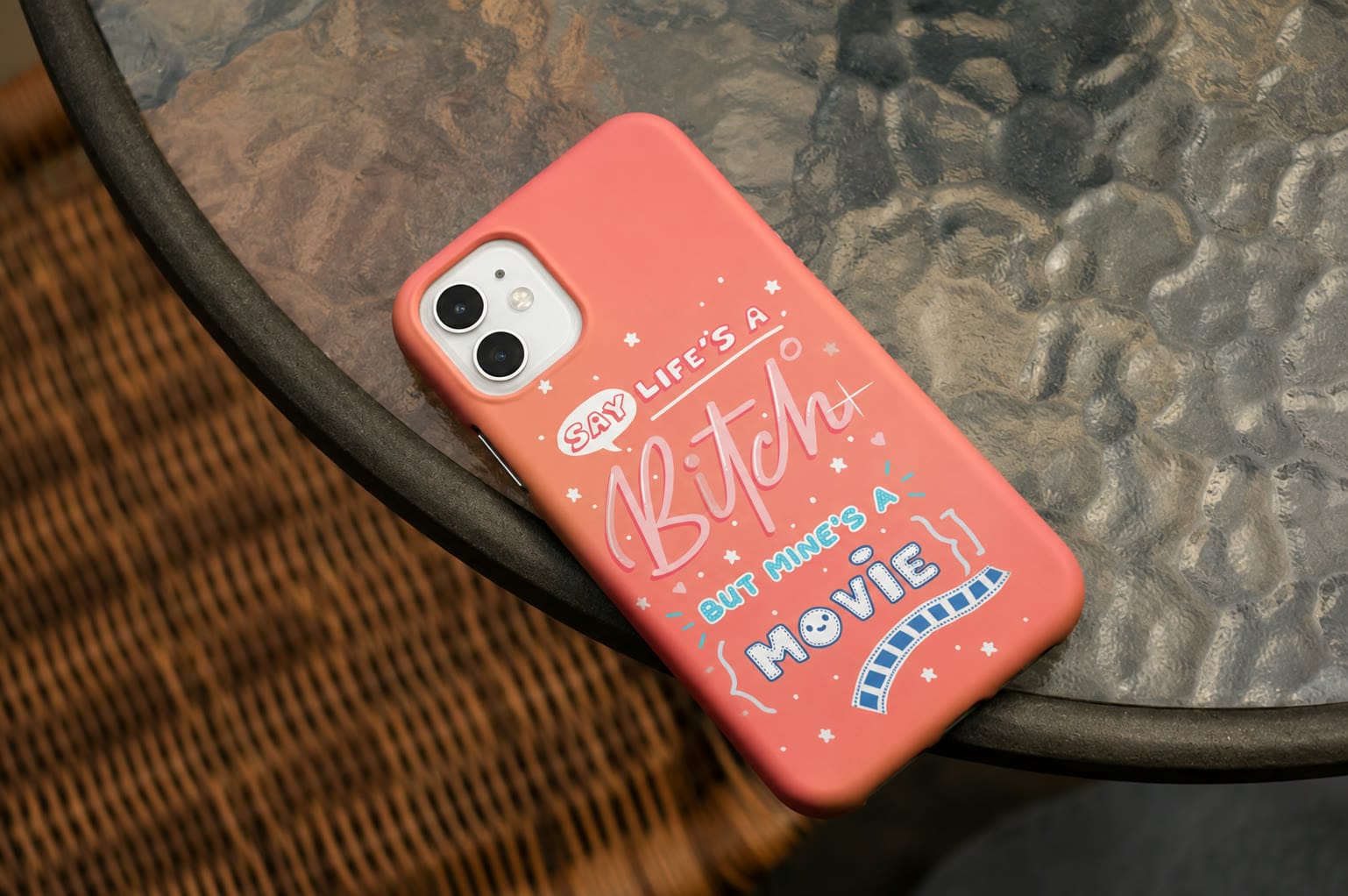 A coral Our Case phone case lying on a woven table top