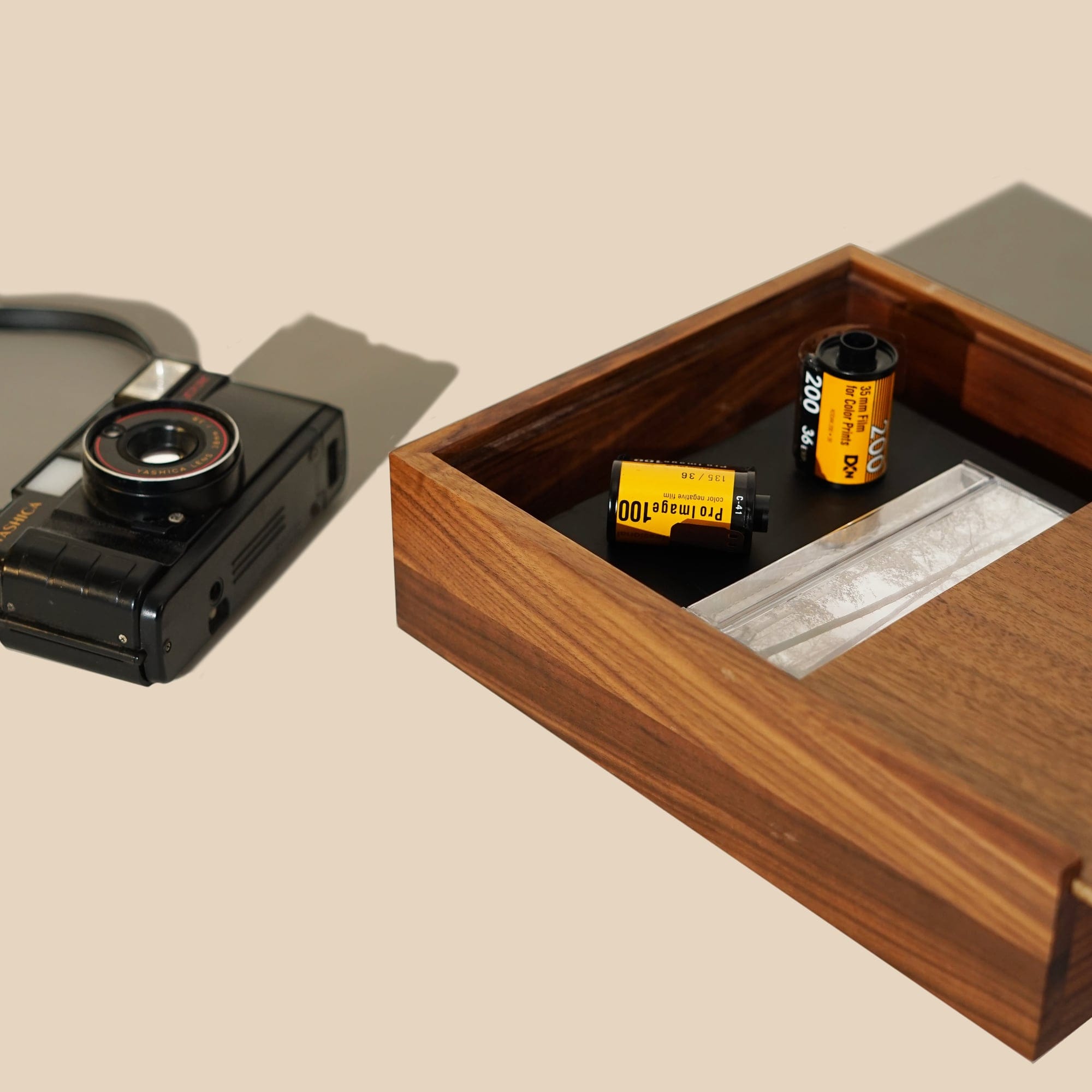 A walnut Memobox tray holding film canisters, a compact camera set beside it