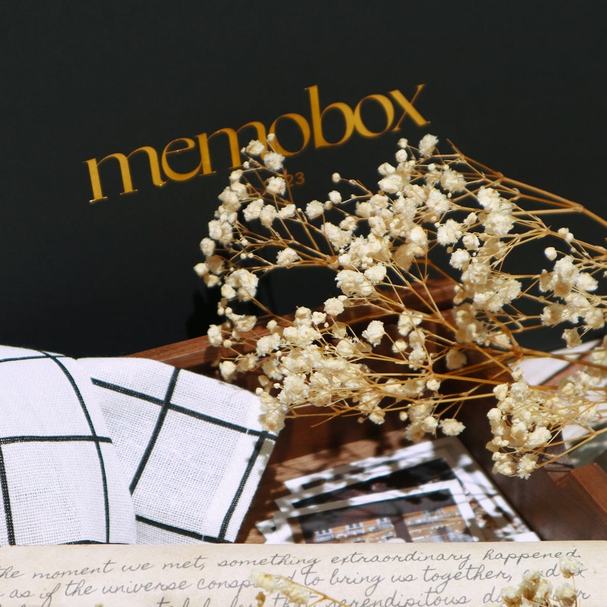 An open Memobox with baby's breath, a checked cloth, photographs and a handwritten note