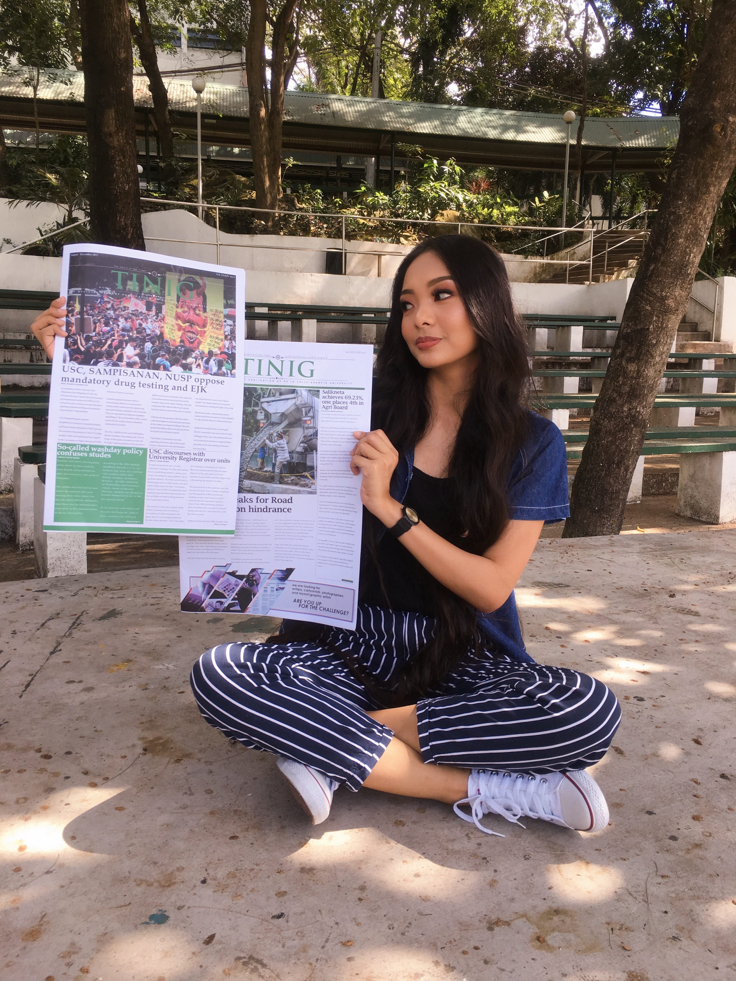 Holding two issues of TINIG, the university paper, on campus